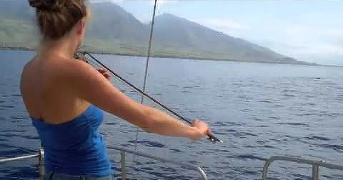 A woman in a blue dress plays violin on a boat, with a whale visible in the water behind her.