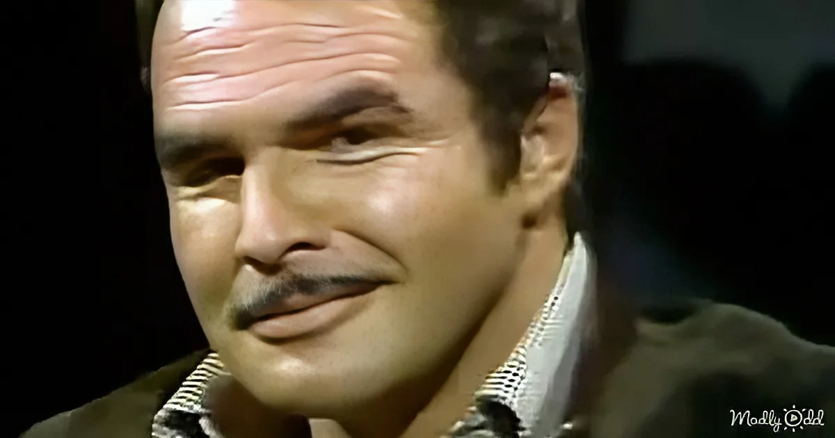 A man with a mustache and a striped shirt is smiling, wearing a dark jacket.