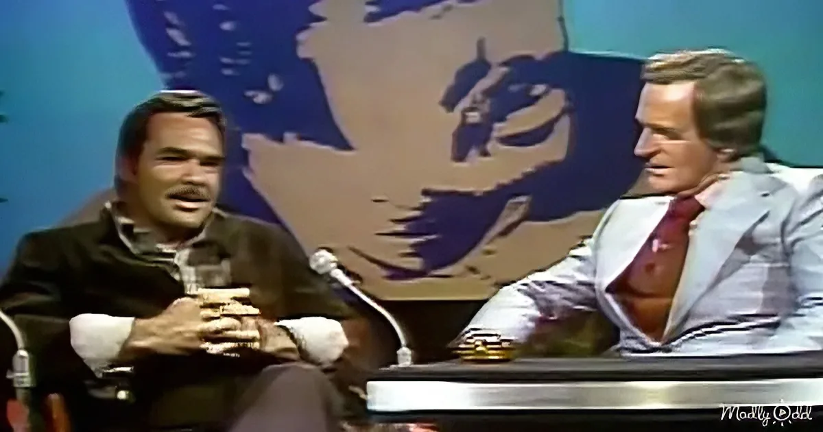 Two men are seated at a table, one in a suit, the other in casual attire, engaged in conversation.