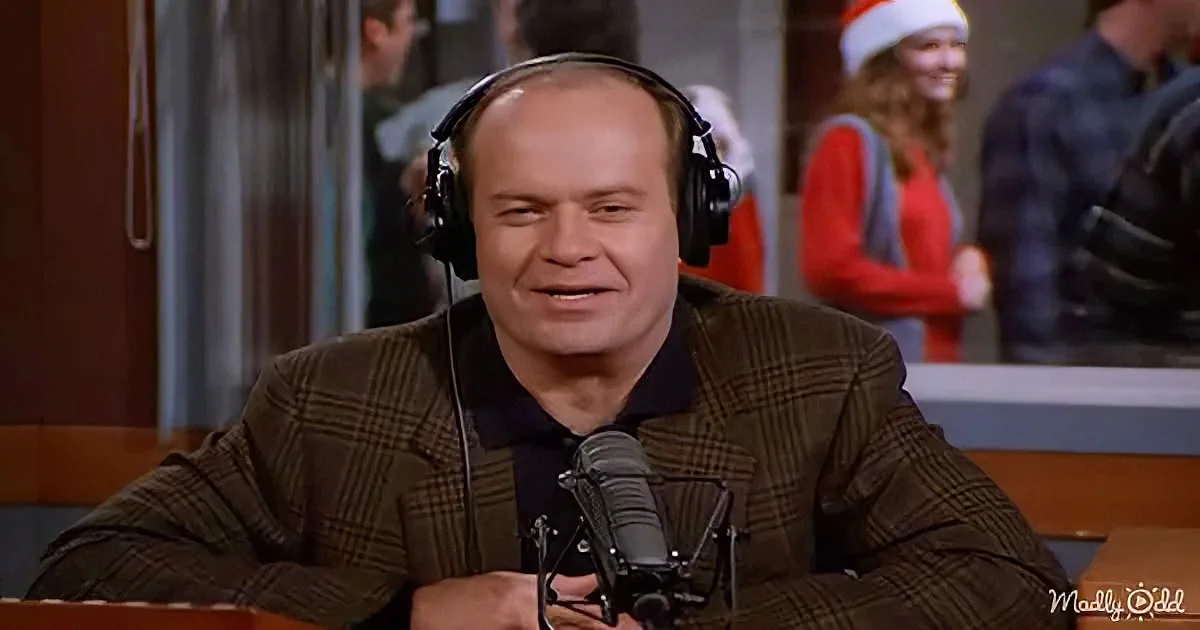A man in a plaid jacket and headphones sits at a microphone, smiling, with a festive background.