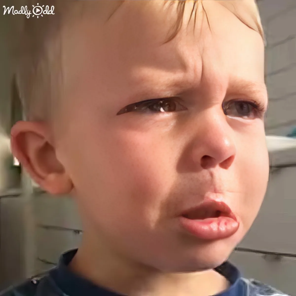 A young child with short blonde hair looks visibly upset, with a tear in their eye and a pouty mouth.