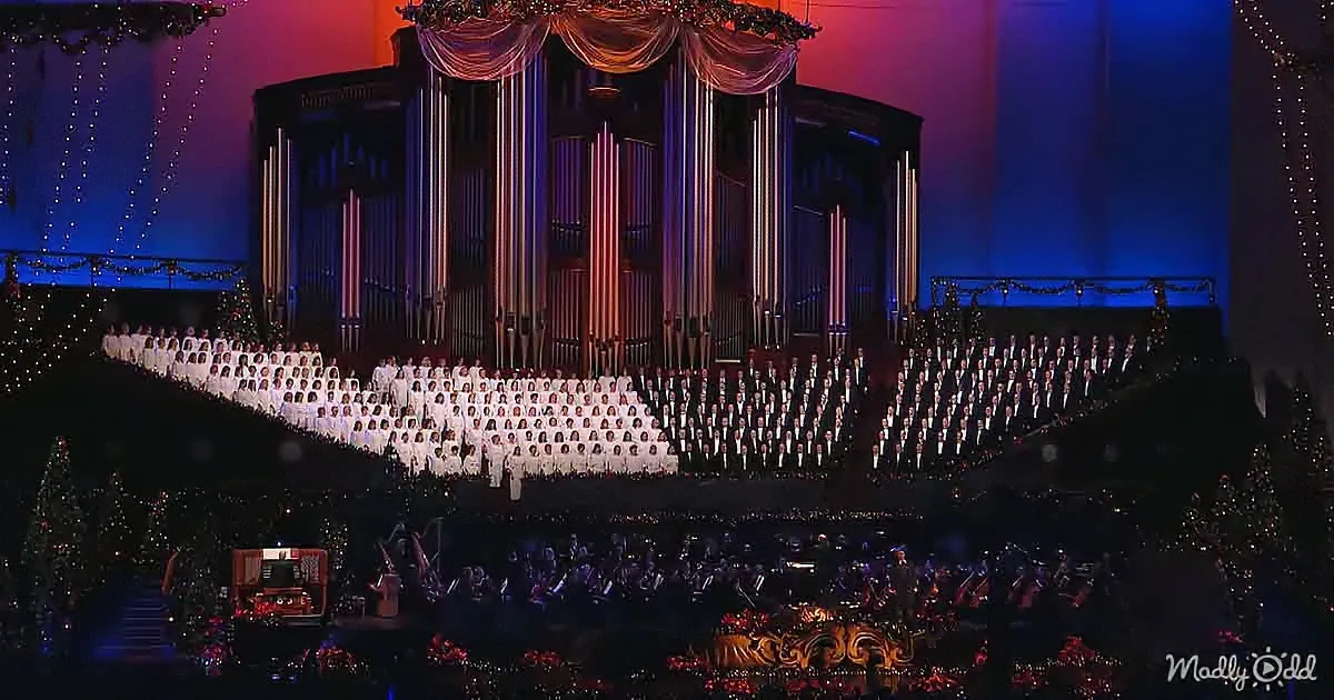 A grand choir in white stands on a stage with a large organ and festive decorations.