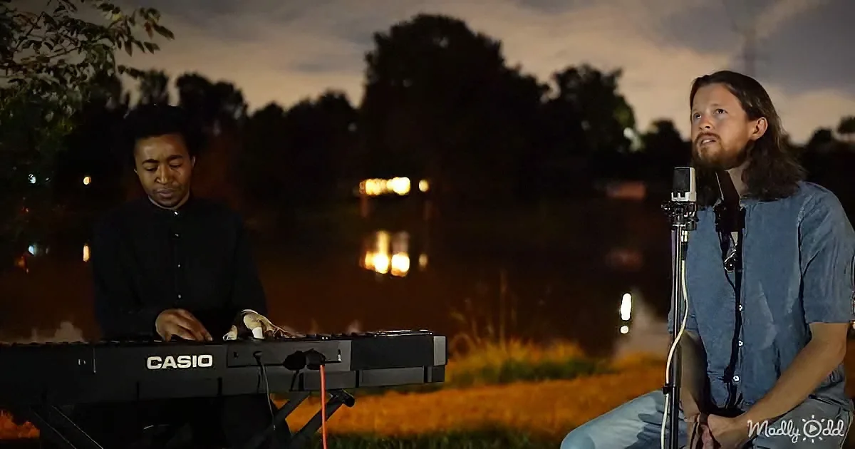A man plays a Casio keyboard while another sings into a microphone near a body of water at night.