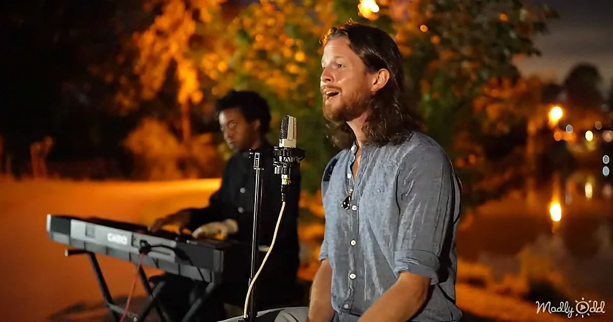 A man sings into a microphone, playing keyboard in the background under a night sky.