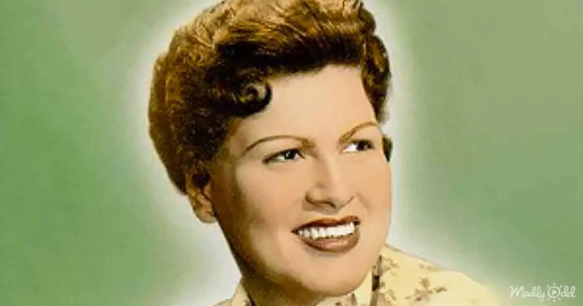 A smiling woman with short, curly brown hair and a light-colored top against a green background.