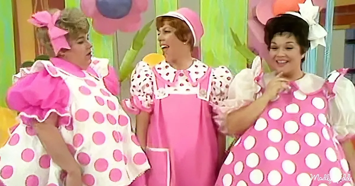 Three women in pink polka-dot dresses and hats are smiling and posing together.