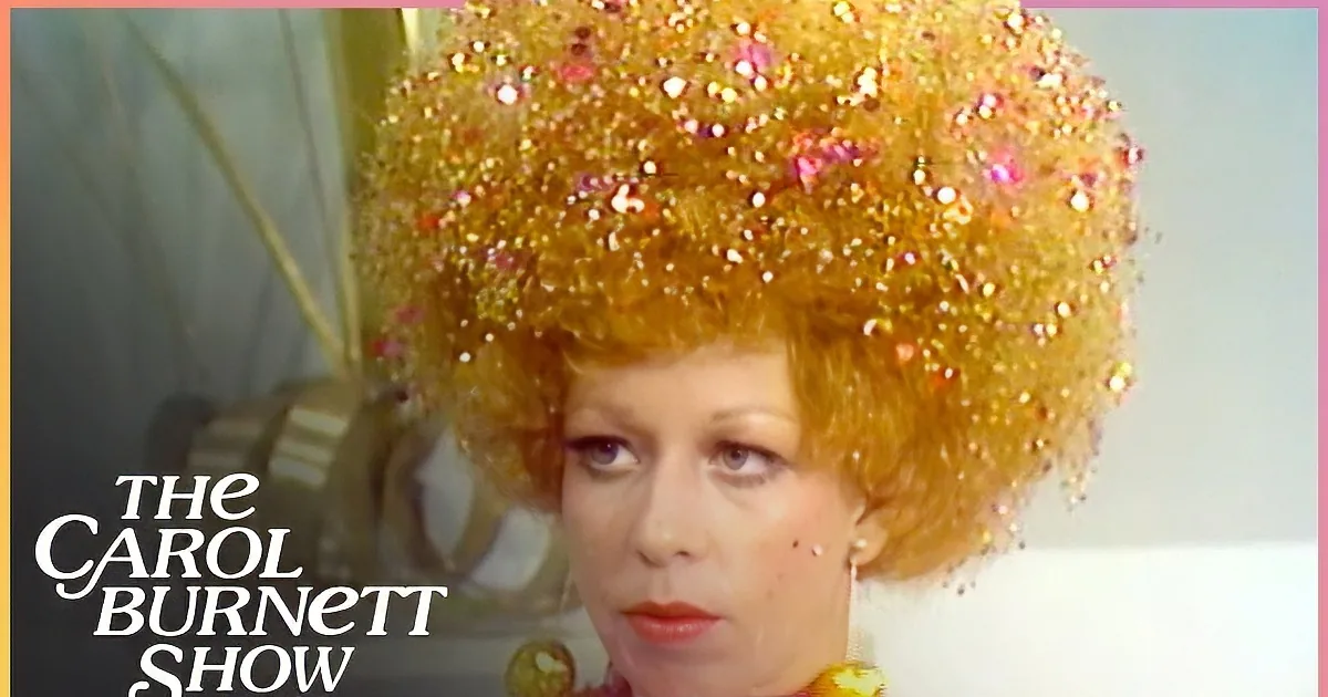 A person with a glittery, large afro wig and colorful sequined outfit is smiling.