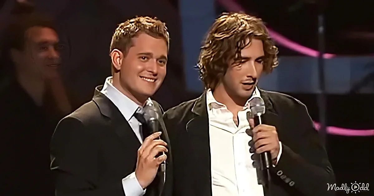 Two men in suits holding microphones, smiling, on stage with a blurred background.