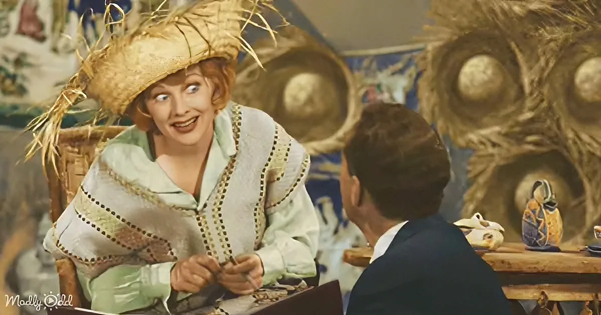 A woman in a straw hat and green outfit smiles while sitting at a table with a man in a dark suit.