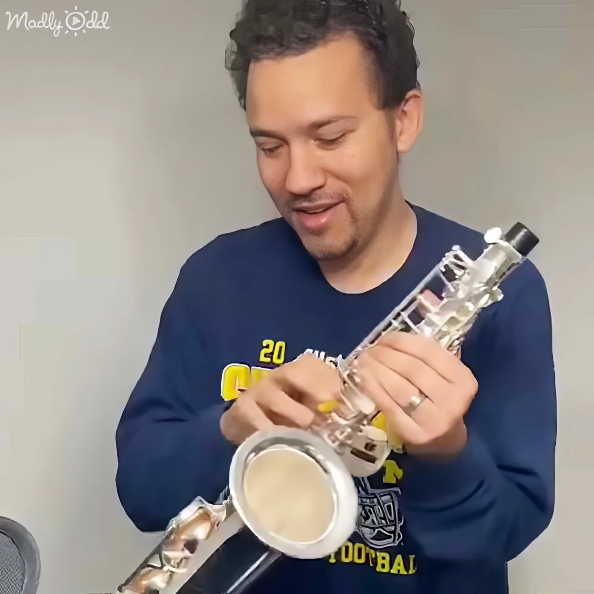 A man in a blue sweatshirt plays a saxophone, focusing intently on his instrument.
