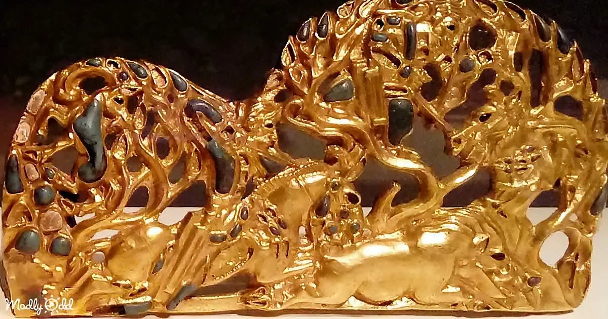 A golden, intricately designed piece with a tree-like pattern and embedded stones is displayed against a dark background.