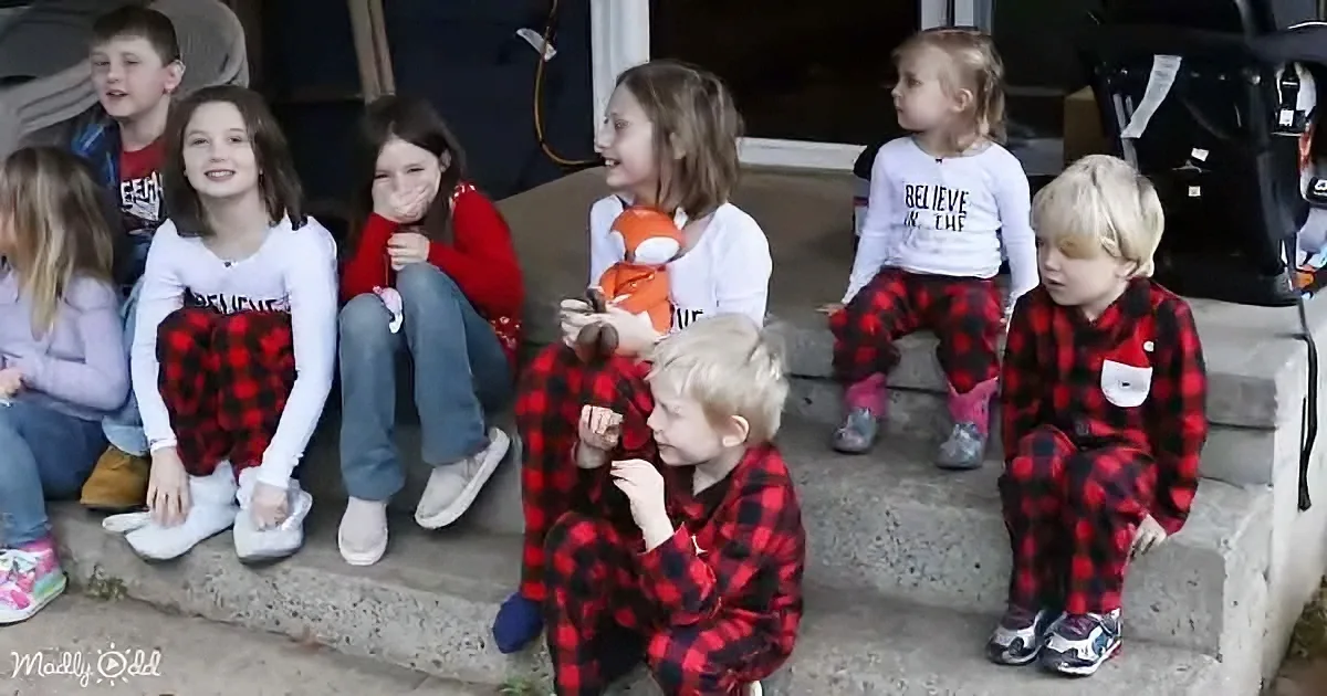 Children in red plaid pajamas and casual clothes sit on steps, some smiling, others looking away.