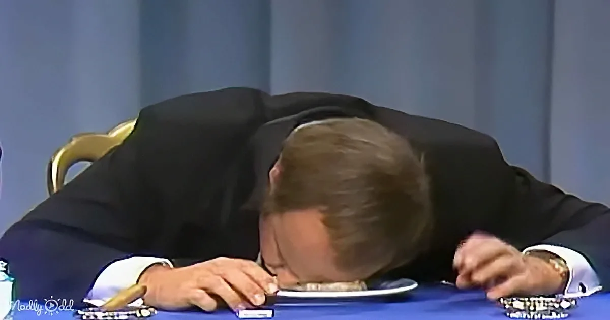 A man in a suit is slumped over a table, appearing to be asleep or extremely tired.