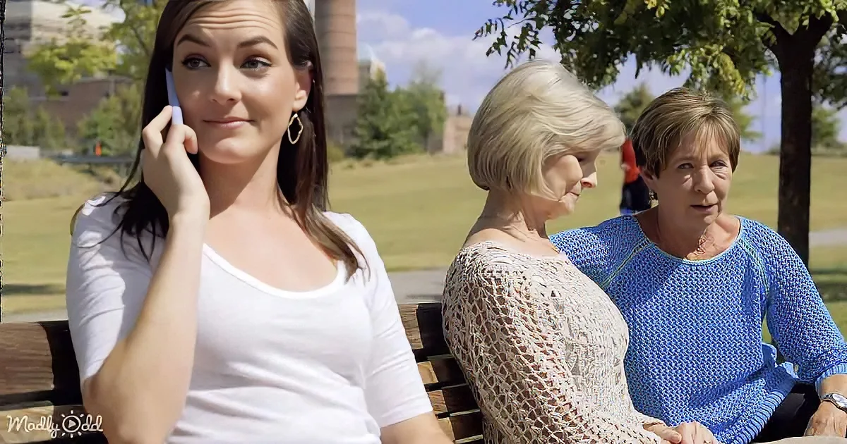 A woman in white talks on her phone while two others sit on a bench, seemingly engaged in conversation.