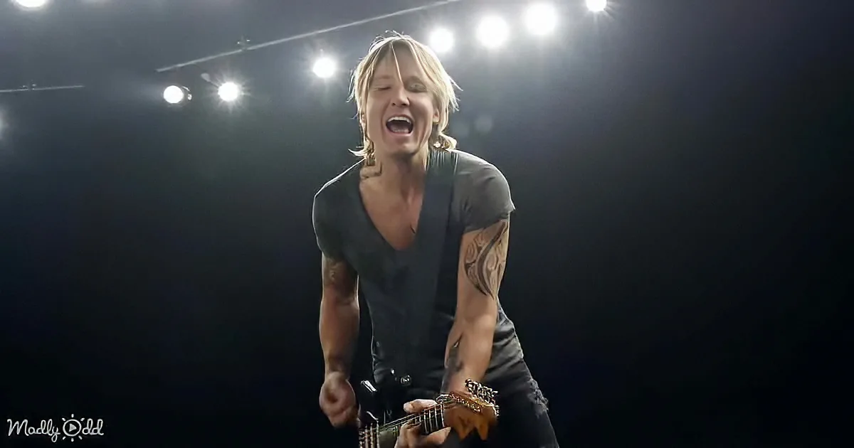 A person with tattoos, wearing a black shirt, passionately plays an electric guitar on stage under bright lights.