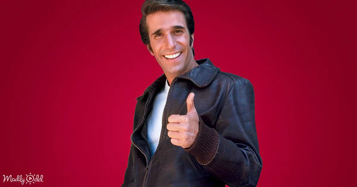 A man in a leather jacket gives a thumbs-up against a red background.