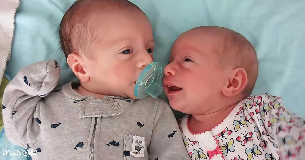 Two newborn babies, one with a pacifier, lying close together on a blue blanket.