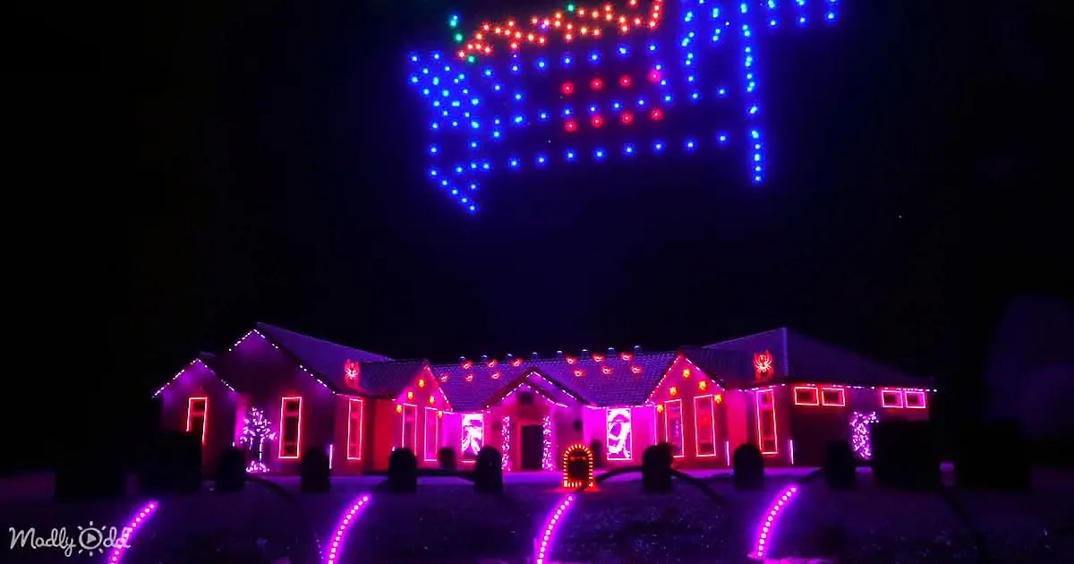 A house adorned with colorful lights, including a large illuminated "Merry Christmas" sign in the sky.