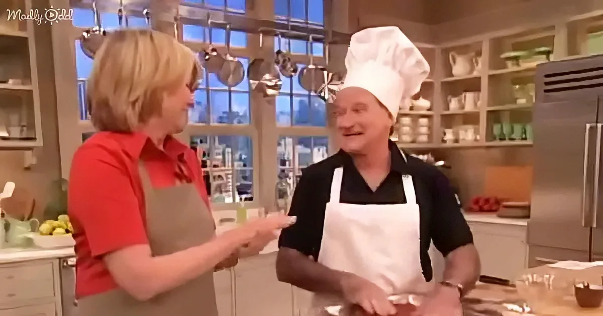 A woman in a red shirt and apron gestures while talking to a man in a chef's hat and apron in a kitchen.