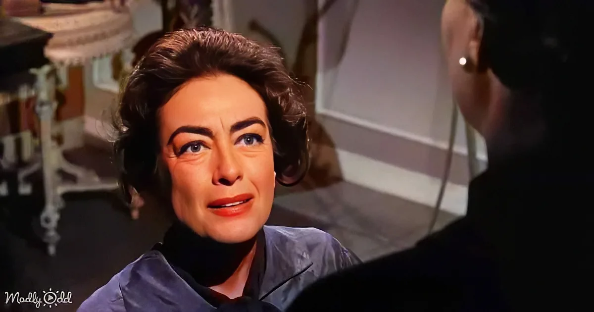 A woman with dark hair and red lipstick is looking up at a man in a dimly lit room.