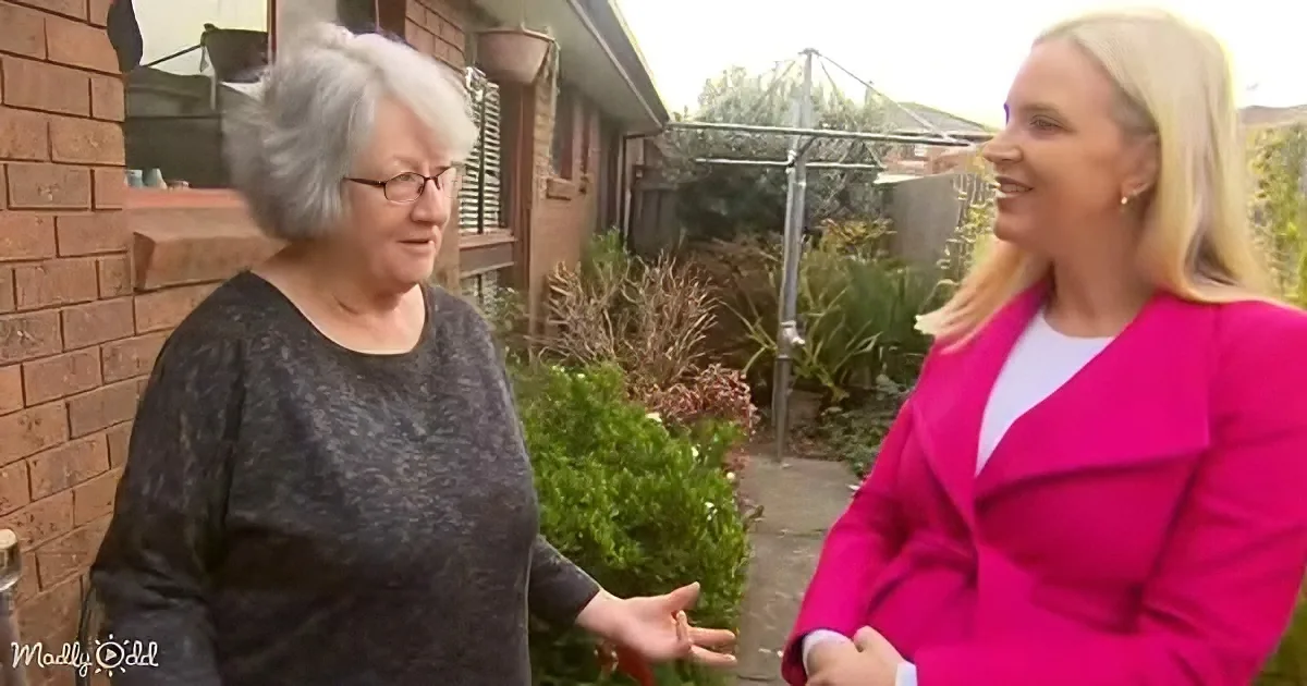 Two women, one in a pink coat, are engaged in conversation in a backyard setting.
