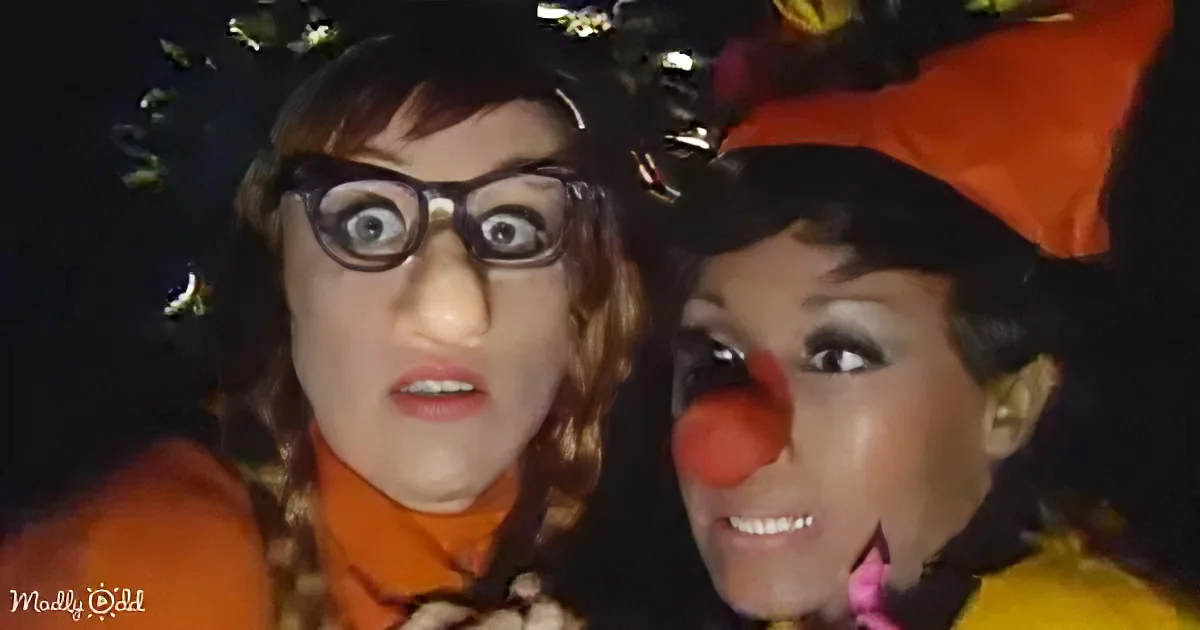 Two individuals in costumes, one with a red nose and the other with a flower crown, posing together.