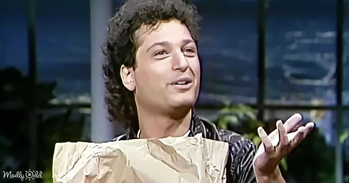 A person with curly hair, wearing a striped shirt and a beige jacket, is gesturing with their hands while speaking.