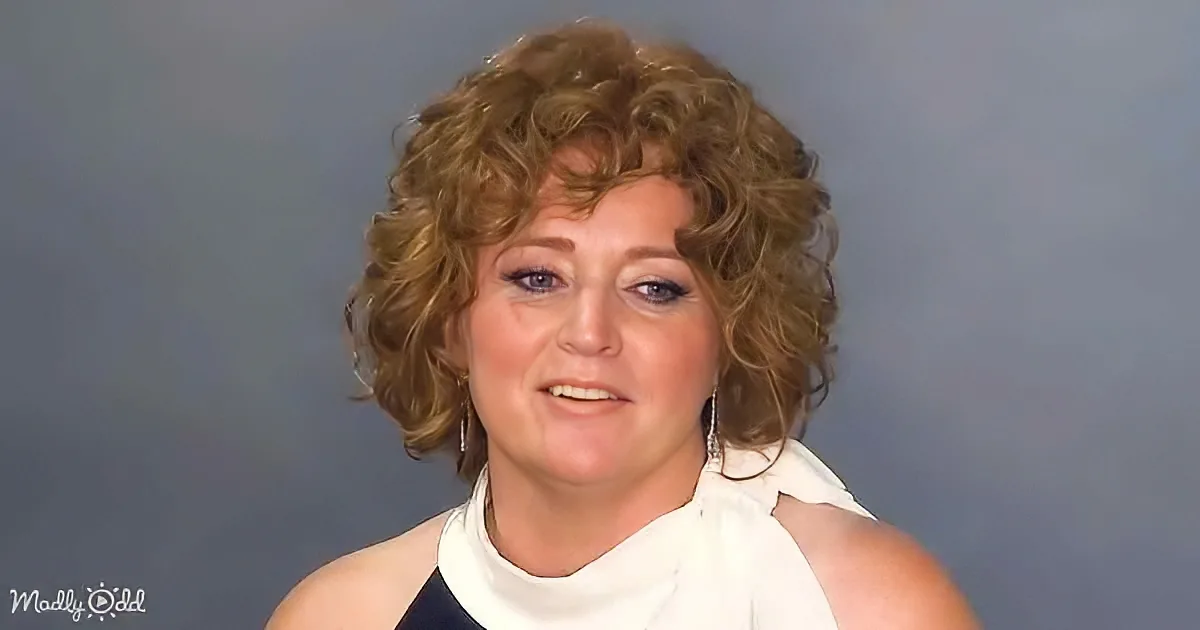 A woman with curly hair, wearing a white top, smiles against a gray background.
