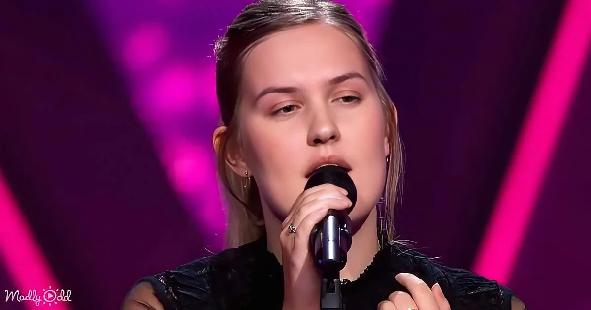 A person sings into a microphone against a vibrant purple background.