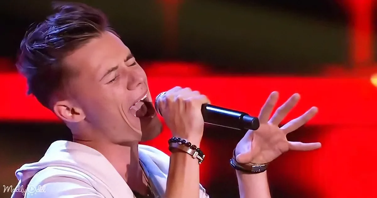 A person in a white shirt sings passionately into a microphone, gesturing with their hand.