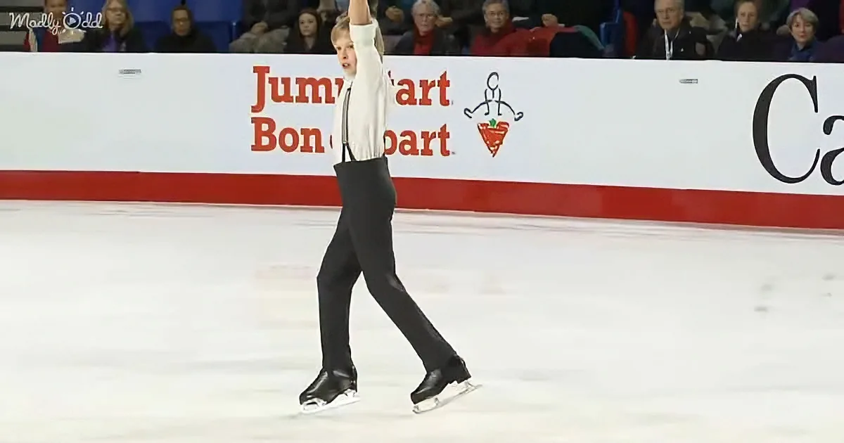 A figure skater in a white shirt and black pants raises one arm while skating on an ice rink.