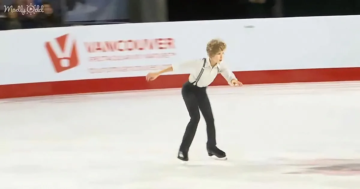 A figure skater in a white shirt and black pants glides on ice, arms outstretched, with a "Vancouver" sign in the background.