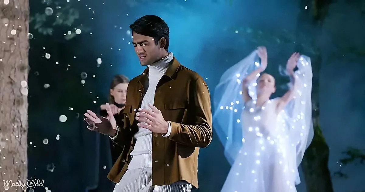A man in a brown jacket and white turtleneck stands with hands clasped, surrounded by glowing figures and a starry backdrop.