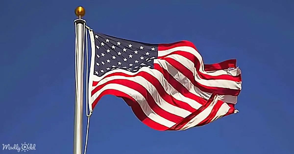 An American flag waves vigorously against a clear blue sky.