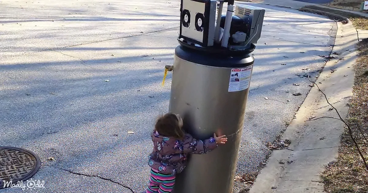 A child hugs a large cylindrical object on a street corner, with a manhole cover nearby.