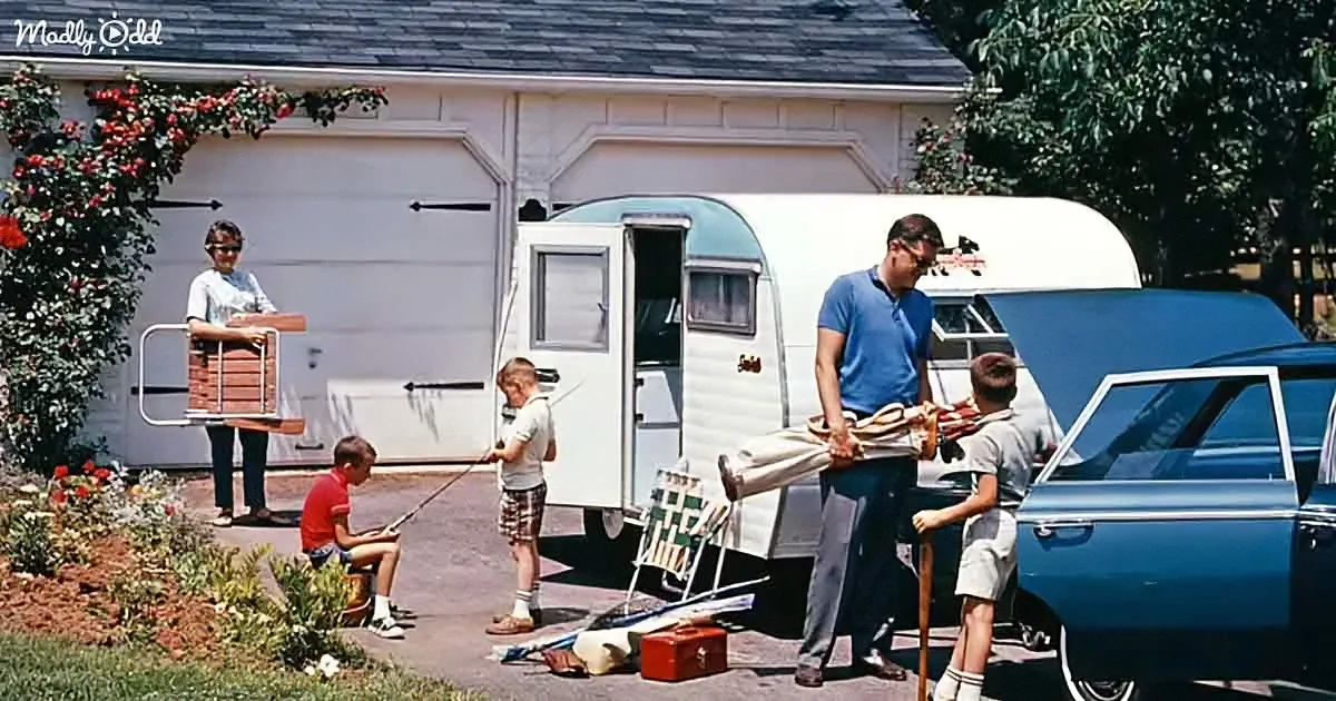 A family prepares for a camping trip, packing gear and setting up near a vintage trailer and car.