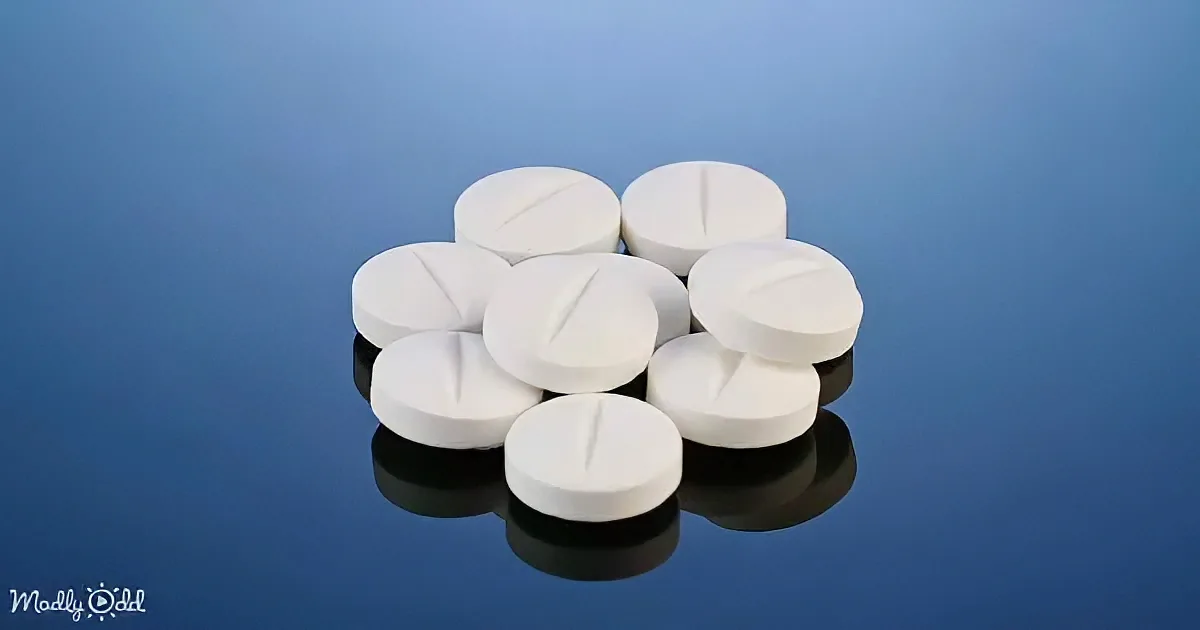 White pills with a central groove are arranged in a cluster on a reflective surface against a blue background.