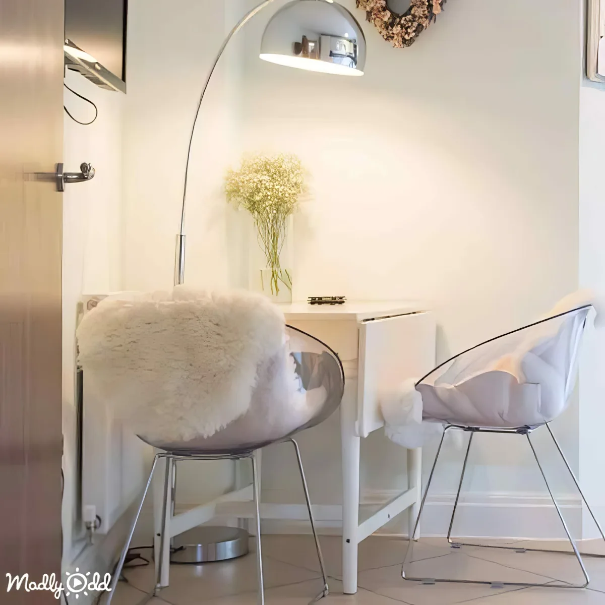 A cozy corner with a white table, two chairs, a floor lamp, and a vase of flowers.
