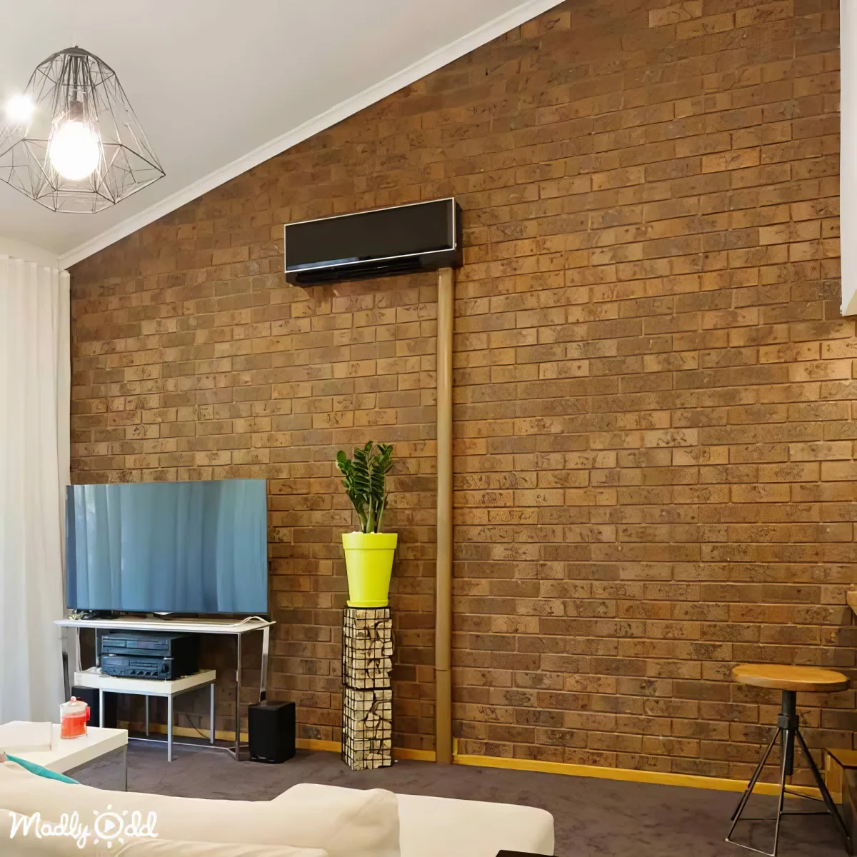 A modern living room features a brick wall, a TV on a stand, a potted plant, and a sleek air conditioning unit.