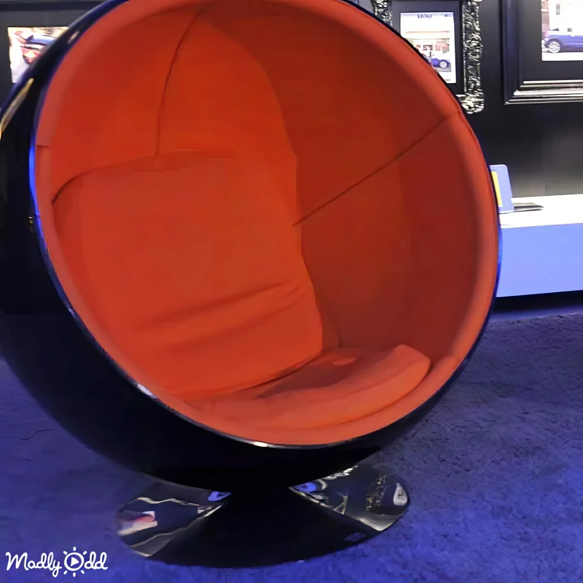 A modern, orange and black spherical chair with a unique design sits on a blue carpet.