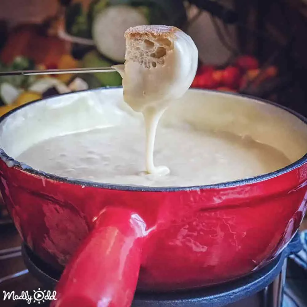 A red fondue pot with creamy white cheese being dipped, surrounded by autumnal decorations.