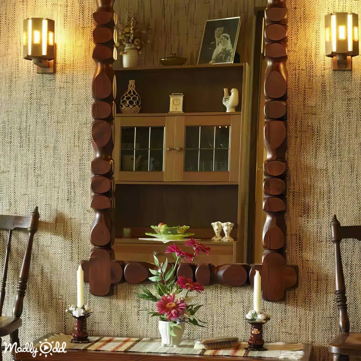 A rustic wooden-framed mirror reflects a dining area with a vase of flowers and a candle holder.