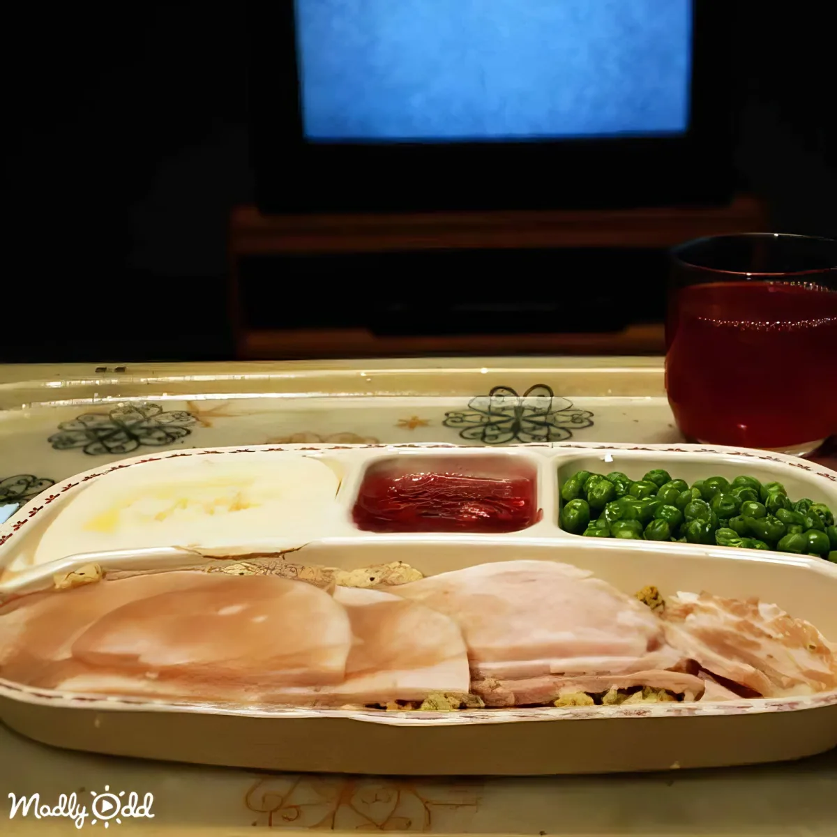 A tray with ham, peas, cranberry sauce, and a drink in front of a TV.