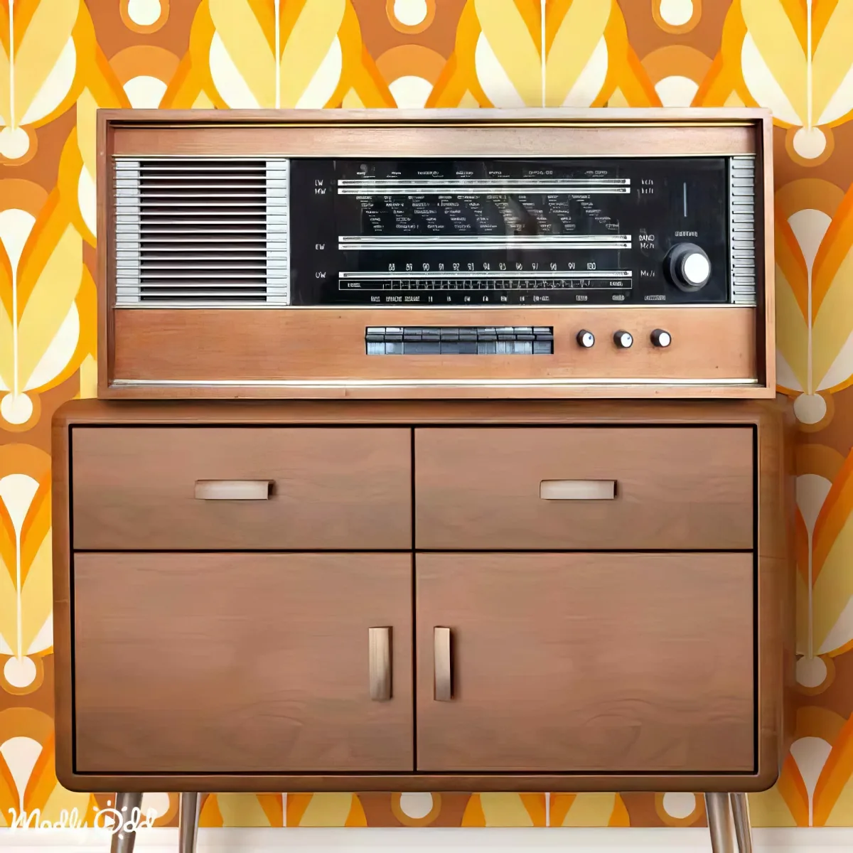 A vintage radio with wooden cabinet sits atop a retro-style cabinet against a colorful, patterned wallpaper.