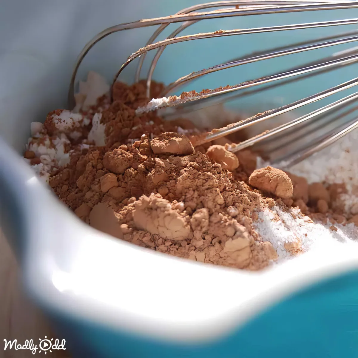 A whisk rests in a bowl filled with cocoa powder and powdered sugar.