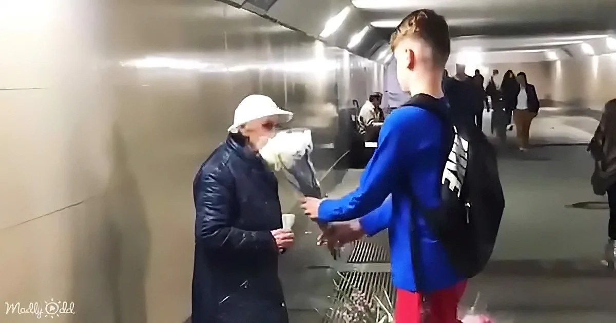 A boy in a blue jacket and backpack hands a bouquet to a woman in a white hat and dark coat.