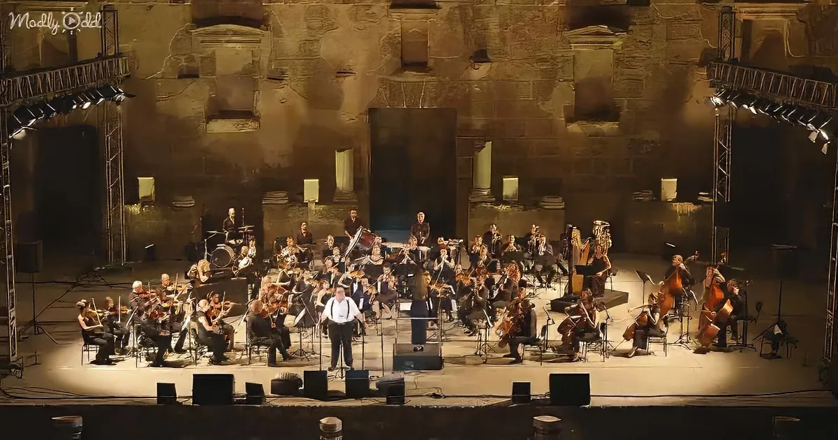 A large orchestra with a conductor on stage in a historic stone venue.