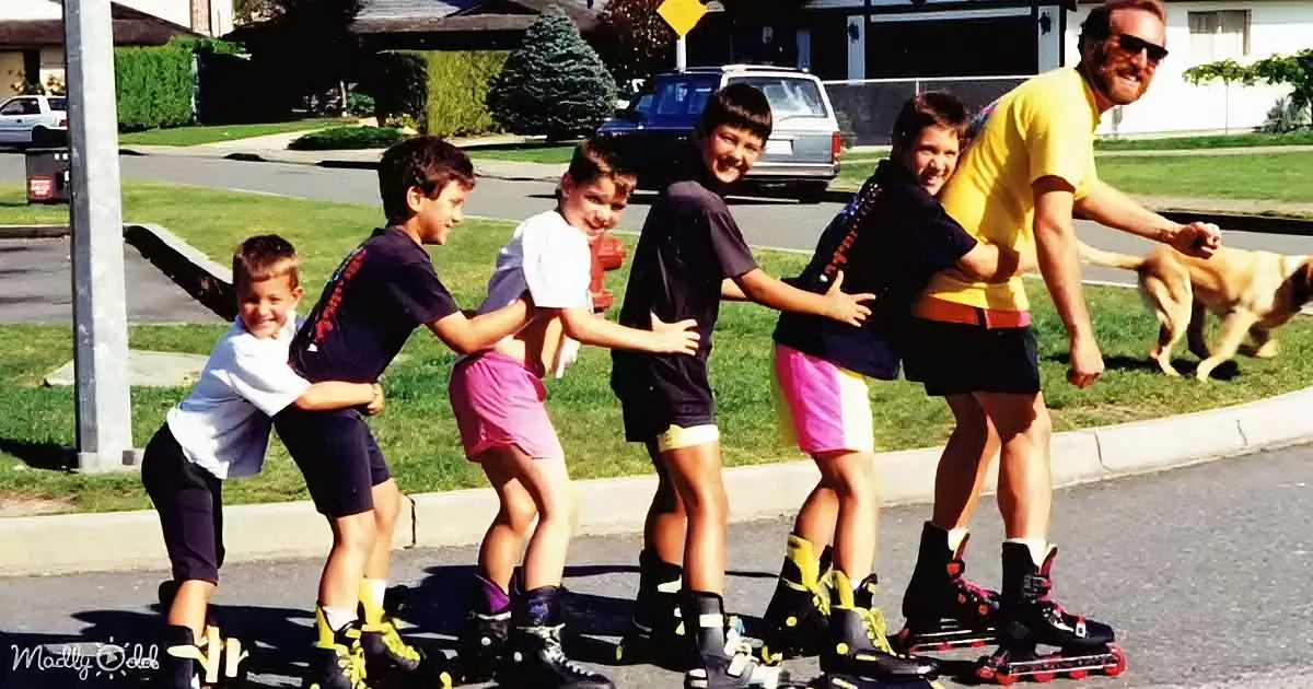 A man and five children roller skate together on a suburban street, smiling and enjoying the moment.