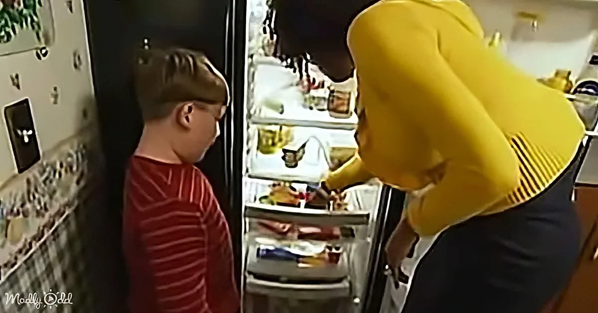 A boy in a red striped shirt watches as a person in a yellow hoodie opens a refrigerator.