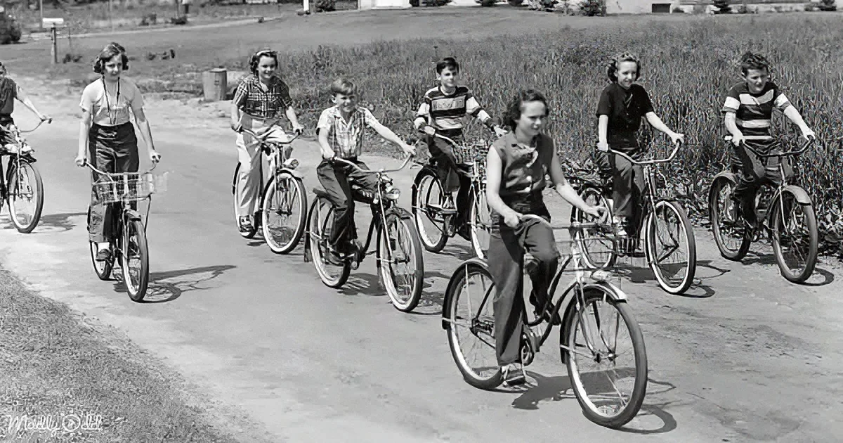Children with bicycles on a paved path, smiling and enjoying a sunny day.